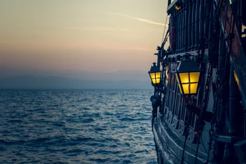 Papier Peint photo Navire Vieux bateau pirate vintage en bois sur la surface de l& 39 eau de mer au coucher du soleil soirée moment romantique avec la lumière jaune de la lanterne à mise au point douce dans l& 39 espace à la mer
