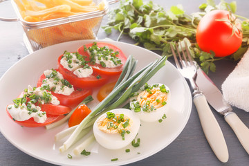 Half boiled eggs with tomatoes, green onions sprinkled with greens in a white plate on a gray wooden table. Close-up
