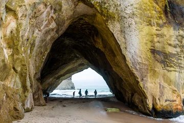 Plexiglas foto achterwand Rock arch in Te Whanganui-A-Hei (Cathedral Cove) Marine Reserve, New Zealand. Silhouette of people near the shoreline. © Roberto