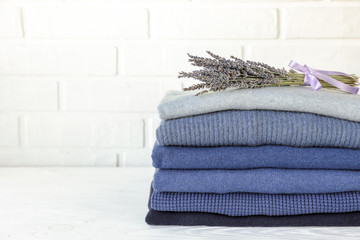 Stack of folded warm knitted men's sweaters in blue and a bunch of dried lavender, care of clothes aroma and protection from moths concept.