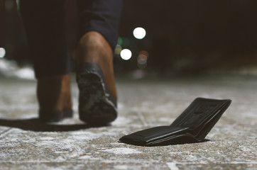 Lost wallet dropped from a woman pocket on the night footpath and is walking away silhouette of...
