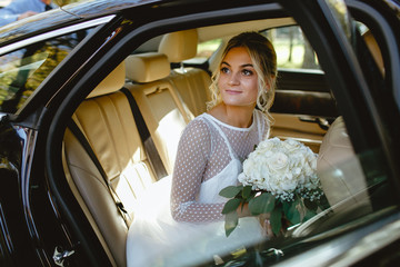 A bride takes pictures in the black car.