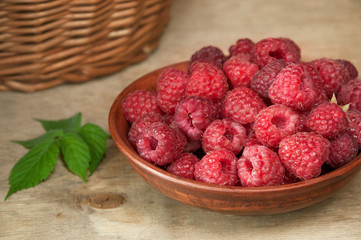 Ripe raspberry berries in a clay plate on a wooden table.
