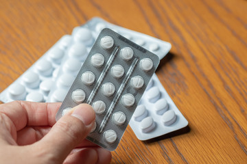 Pharmaceuticals antibiotics pills medicine and healthcare concept. Close up man hand holding pills or tablets in blister packs on wooden table.