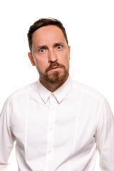 Obraz premium Portrait of handsome man with stubble has indignant expression, frowns face, dressed in white shirt, isolated over white background.