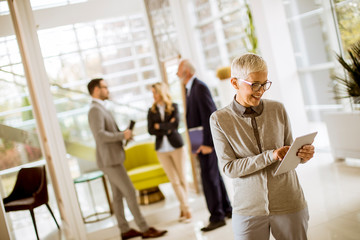 Portrait of senior businesswoman with digital tablet while other business people standing in background