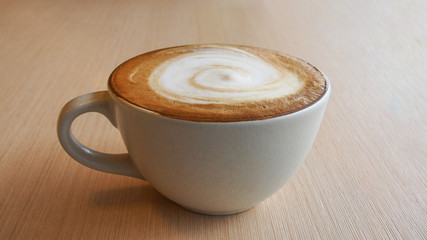 Hot coffee cappuccino latte in ceramic cup with spiral milk foam on plywood table background.