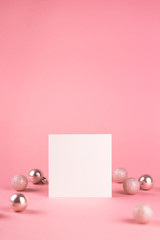 Mock up with square invitation card on trendy pastel light pink background with christmas ornaments. Greeting card and silver Christmas baubles. Minimal christmas concept.