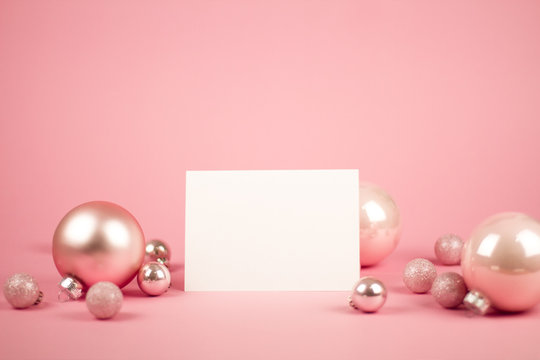 Mock up with invitation card on trendy pastel light pink background with christmas ornaments. Greeting card and silver Christmas baubles