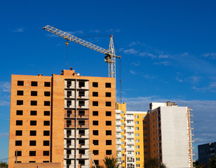 Fototapeta na wymiar Brick multistory building under construction with crane on the site, blue sky background
