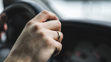 Men driver's hand with wedding ring on the steering wheel. Close up