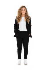 Smiling girl with curly blonde hair, she is standing with hands in pockets, wearing a black suit and white shirt and sneakers