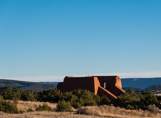 Ruins of an old adobe Spanish mission church set in a landscape of grassy meadows, trees, and mesas...