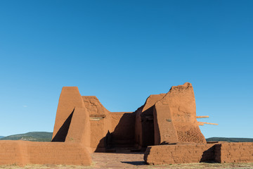 Ruins of an old adobe Spanish mission church under a vast blue sky in Pecos National Historical...