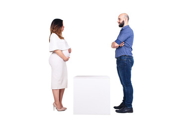 A pregnant woman and a bearded man are seriously looking at each other, and between them is an empty white pedestal