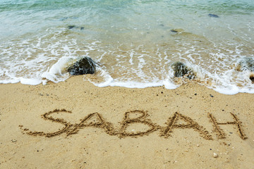 Sabah word on a sand beach with waves - travel concept, Malaysia.