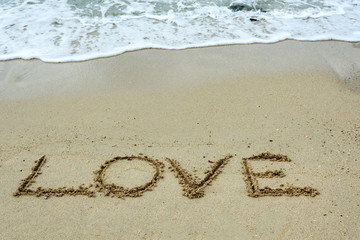 Love text on a sand beach with waves.