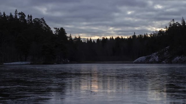 Time-lapse of sunrise and clouds moving, with light reflecting on the ice of a frozen lake. Camera pan upwards.