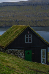 Obraz premium Scenic landscape view of traditional historic stone wooden house/building with grass (turf) roof in Gasadálur village, Vágar Island. Tourist popular attraction/place in Faroe Islands (Denmark)