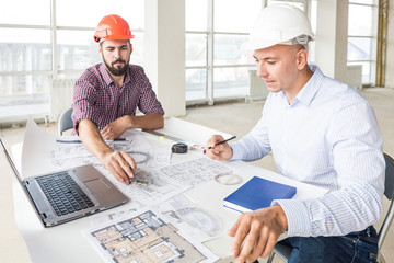 male engineers, architects working at the desk in helmets. Drawings, laptop, roulette on the desktop. Reception and supervision of building construction