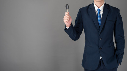 Business man is holding car key, grey background in studio