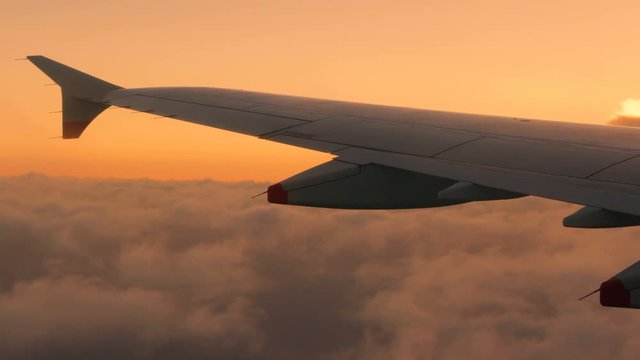 Passengers view of an airplane wing as the plane soars in high altitude during sunset under a blanket of volumetric gray clouds