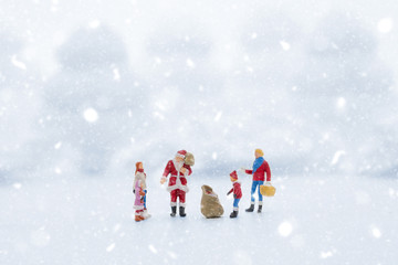 Miniature people in Christmas Theme. Santa Claus giving Christmas gift to children on Christmas day