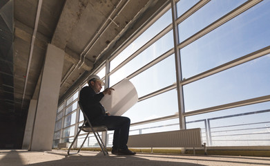 the builder architect in a helmet with drawings is working at the construction site. supervision of construction. silhouette by the window