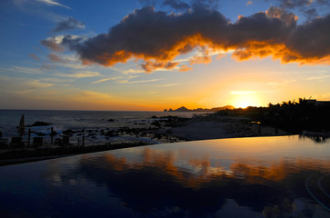Sunset over a reflective swimming pool on a Cabo San Lucas beach. 