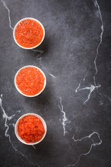 Red caviar Three species of salmon caviar in a white bowl on a black marble background. Variety of tastes.Seafood. Healthy Food Concept. Snack.Copy space for Text.