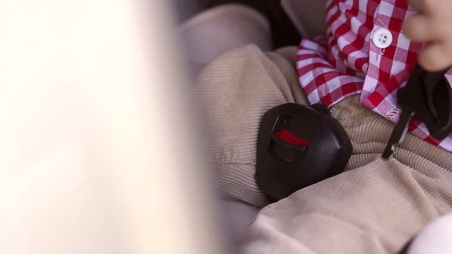 Close-up of a little boy unbuttoning his seat belt in a child car seat. Slow motion.