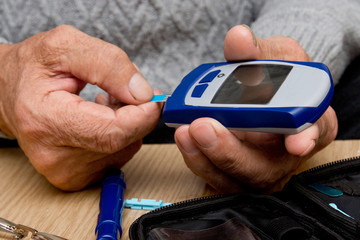 Concept diabetes in the elderly retired. Senior man with glucometer checking blood sugar level at home. Learn to use a glucometer