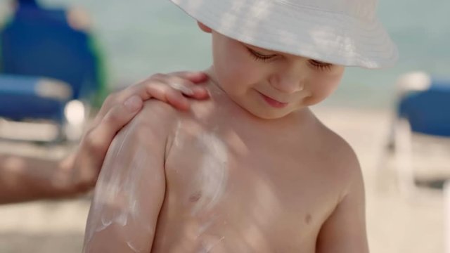 Close-up Portrait Of Confident Little Boy Wearing Hat During Mother Female Hand Applying Sunscreen Cream Or Lotion On Body Skin Of Child Mom And Kid Enjoying Seaside Vacation