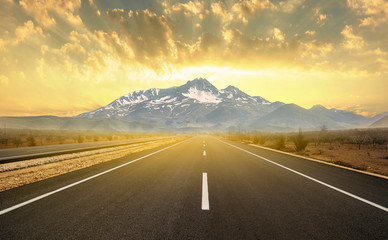 Asphalt road leading to mountain at sunset. 