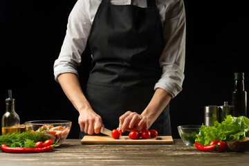Professional chef slices cherry tomatoes for shrimp with vegetables,the concept of seafood and healthy food. Horizontal photo, menu, recipe book