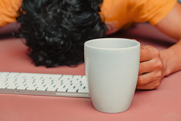 Man has burn out at work. Head, keyboard, smart phone and coffee on pink table