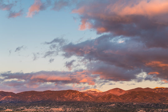 Dramatic, beautiful sunset casts purple and orange colors on clouds and mountains over a neighborhood in Tesuque, near Santa Fe, New Mexico