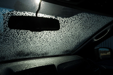 Frozen car windshield with the sun shing thru on a cold winter morning and ice crystal formed on...