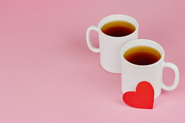 Red paper heart and two white cups on pink background. Valentine's day, love, wedding concept