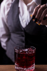 Bartender making refreshing coctail on a bar background. Dark moody style. Ice in tha glass