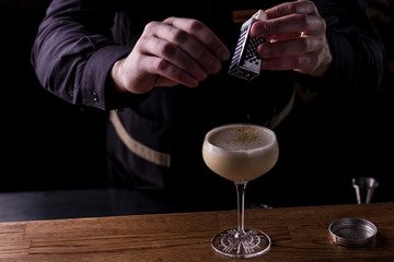 Bartender making refreshing coctail on a bar background. Dark moody style. Ice in tha glass