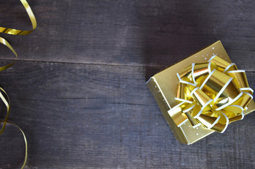 gold box with a gift for Christmas with gold ribbon and bow for a birthday or holiday on a brown wooden background
