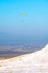 Paraglider flying over white terraces with turquoise thermal water pools
