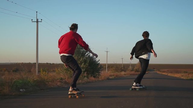 Friends skateboarding riding on empty road at sunset rapid slow motion