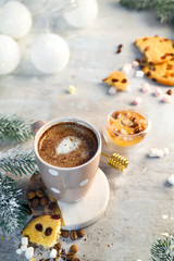 Hot cappuccino with marshmallows in a ceramic cup with honey and metal honey stick on a wooden dark background with Christmas tree branches and Christmas decorations