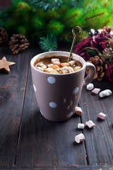 Hot cappuccino with marshmallows in a ceramic cup with honey and metal honey stick on a wooden dark background with Christmas tree branches and Christmas decorations