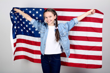Young girl holding an American flag on grey background