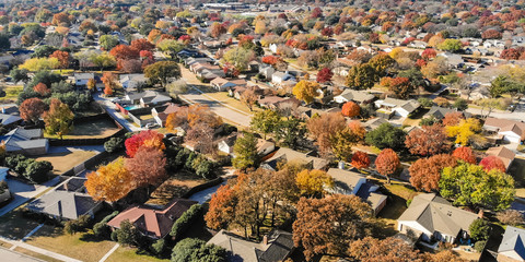 Panorama top view beautiful neighborhood in Coppell, Texas, USA in autumn season. Row of single-family home with attached garage, garden, surrounded by colorful fall foliage leaves under blue sky