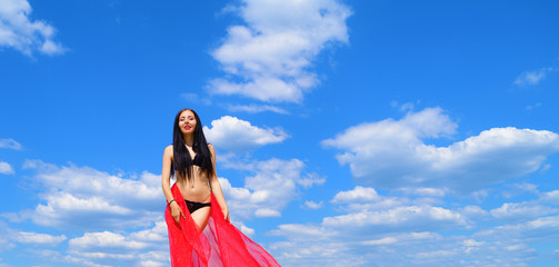 Young brunette girl in black lingerie with red canvas on sky background with clouds.