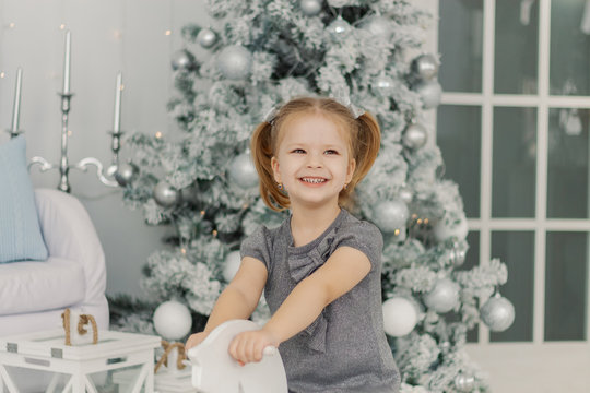 beautiful little girl in a white dress like a princess is sitting on a toy wooden horse in a vintage studio, New Year and Christmas photography.